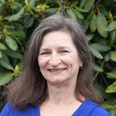 Hansen Dentistry Staff Member Carol Smiling In Front Of Shrub