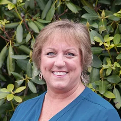Hansen Dentistry Staff Member Trish Smiling In Front Of Shrub